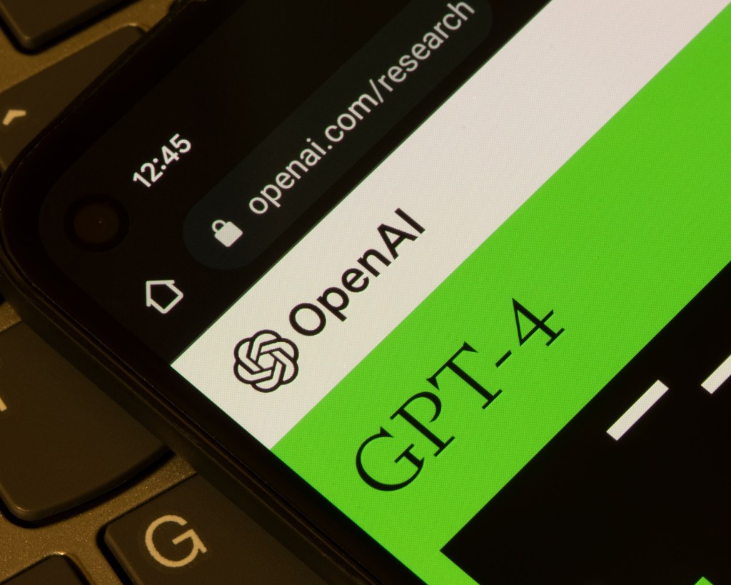 close up shot of an iphone screen with OpenAI and GPT-4 open. Laptop keyboard is in the background.