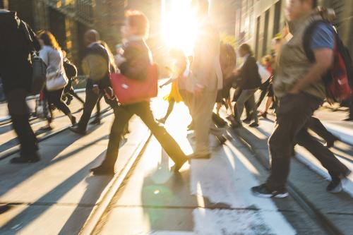 Blurred people crossing the street. Background ready image with fast moving people walking across the road with sun flares in the middle. Travel and commuting concepts