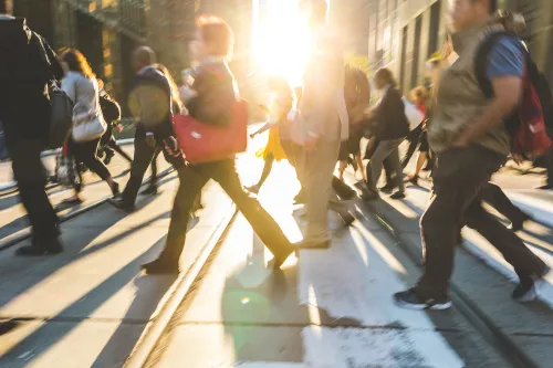 Blurred people crossing the street. Background ready image with fast moving people walking across the road with sun flares in the middle. Travel and commuting concepts