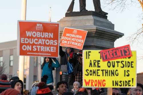 Children support their teachers and parents on strike by holding signs on a Civil War monument during a rally in Woburn, Massachusetts. Schools in Woburn, Massachusetts remained closed for a third straight day as teachers continued to picket strike lines and negotiate contracts with the city of Woburn, Massachusetts.