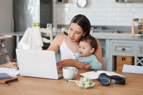 Playing some music in the background is the only way shell sit still. a mom working on her laptop with her baby on her lap.