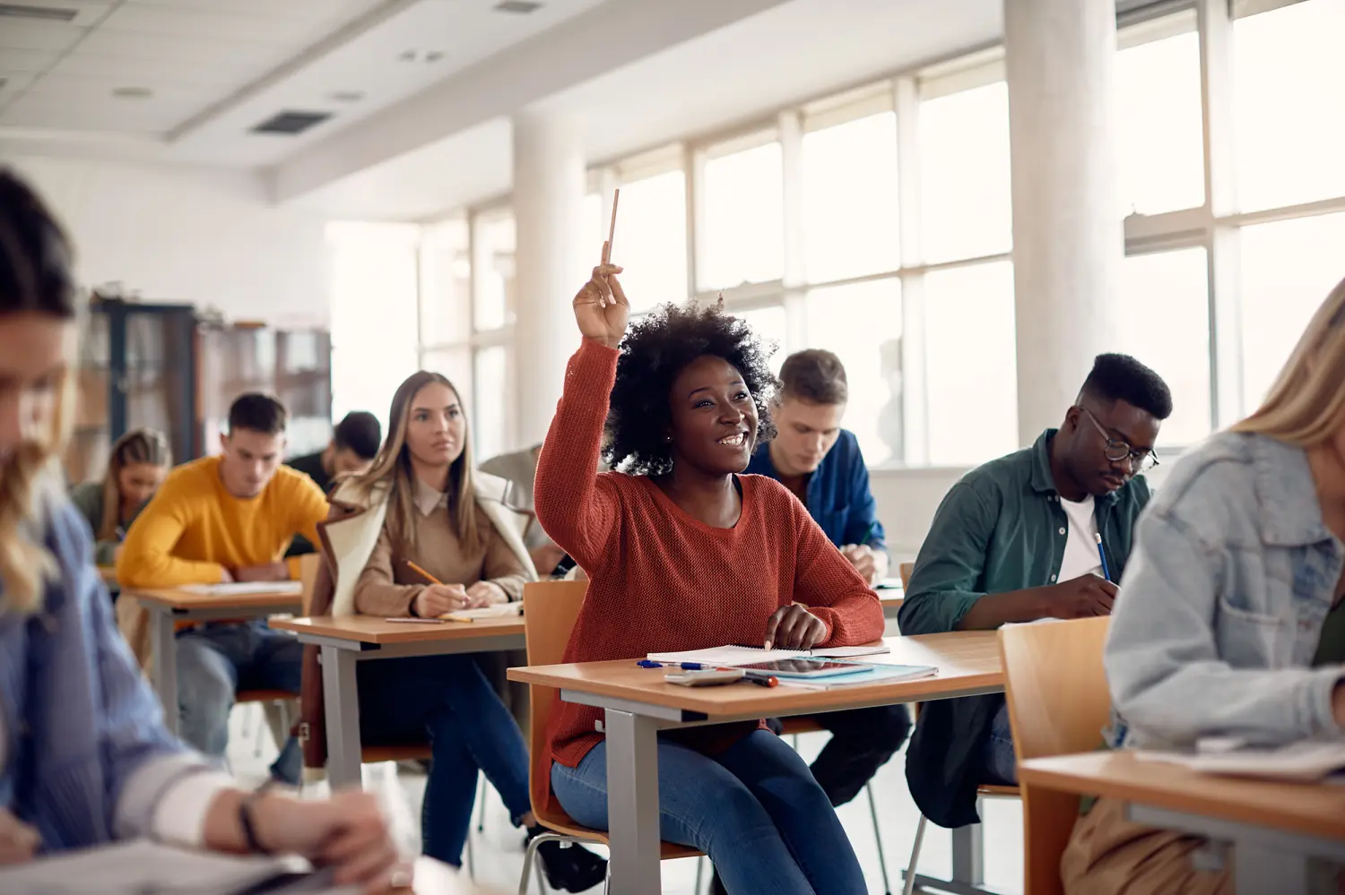 Happy Black student raising her hand to ask a question during lecture in the classroom.