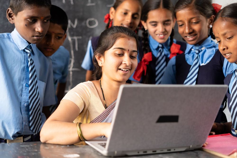 Female teacher and students gathered around a laptop in India