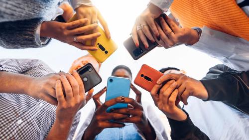 Teens in circle holding phones. Shutterstock/DavideAngelini