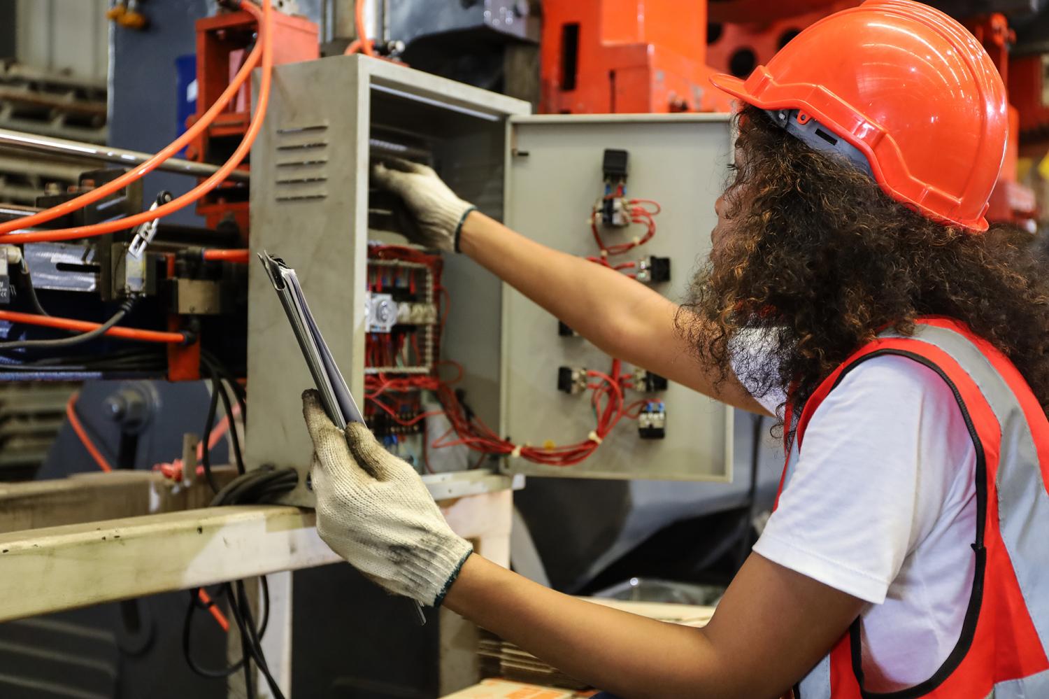 a young female electrician operating on metal machine tool in factory or machinery industry