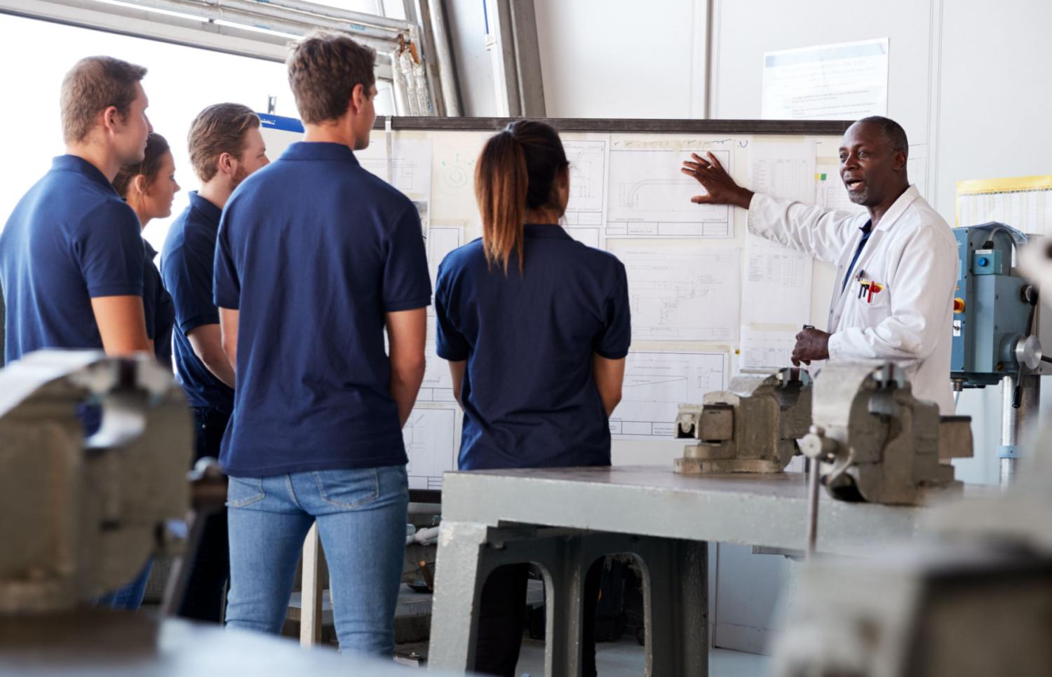 Adult students listening to an instructor lecture at a whiteboard