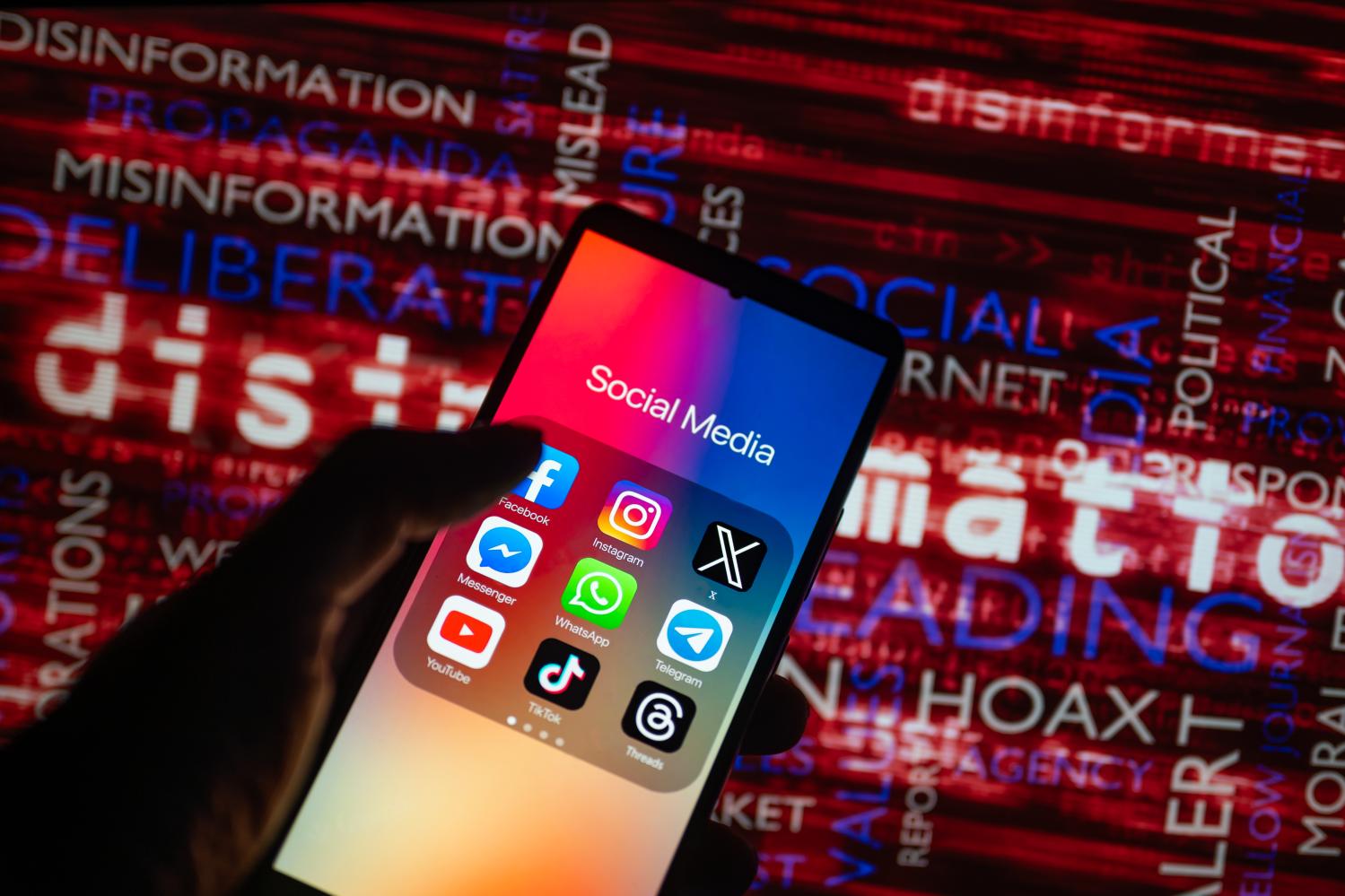 Social media icons logo displayed on a smartphone with disinformation on screen seen in the background, in this photo illustration.