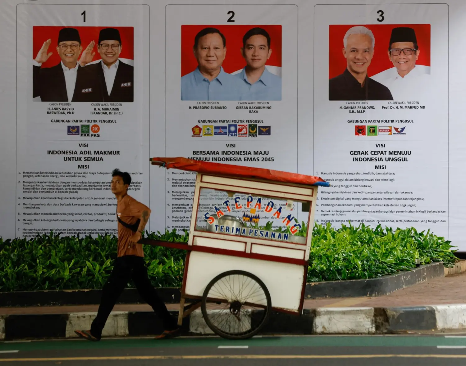 Street vendor pulls cart past banner of Indonesia's presidential candidates