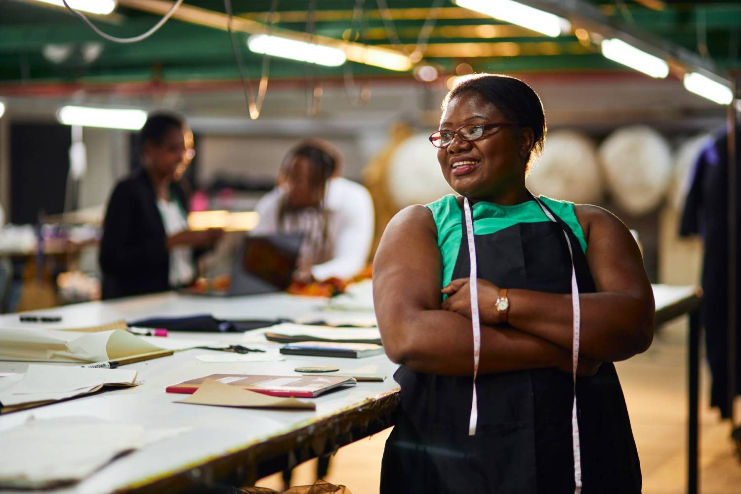 A young African woman stands with her arms folded in a textile workshop. (Photo credit: Magnifical Productions / Shutterstock)