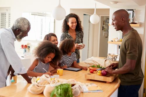 Grandparents Sitting At Table With Grandchildren Playing Games As Family Prepares Meal