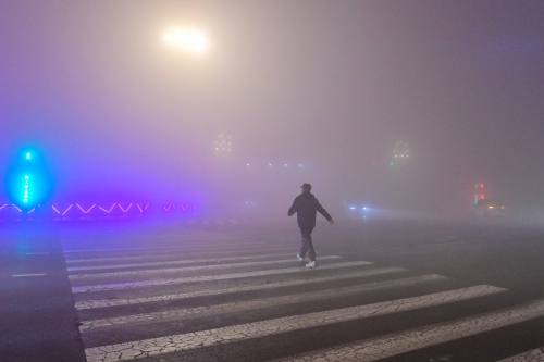 A man walks in a crosswalk on a foggy street.