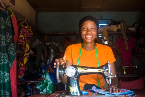 young African woman who is a tailor working on a dress smiling