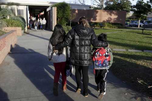 A mother escorts her children on to the campus of Beethoven Street Elementary School in Los Angeles, California on December 16, 2015.
