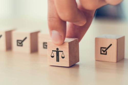 A hand grips a wooden cube printed with the scales of justice