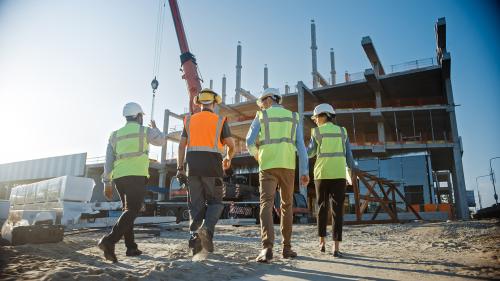 Diverse Team of Specialists Inspect Commercial, Industrial Building Construction Site. Real Estate Project with Civil Engineer, Investor and Worker. In the Background Crane, Skyscraper Formwork Frames