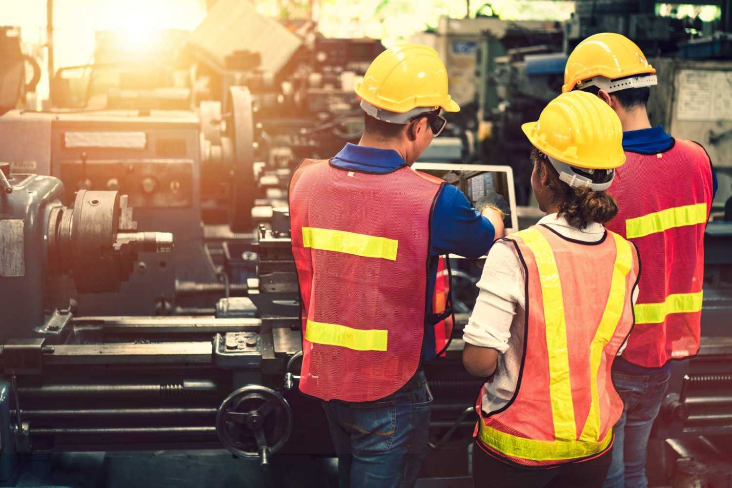 Workers wearing safety gear stand in front of large machinery