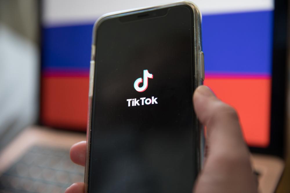 A man holds a smartphone with the TikTok app in front of the flag of the Russian Federation. Photo by Michael Kuenne/PRESSCOV/Sipa USA