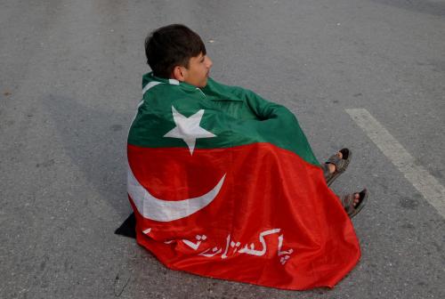 A supporter of Pakistani former Prime Minister Imran Khan's party, the Pakistan Tehreek-e-Insaf, wrapped in the party flag, sits on a road as demonstrators block the Peshawar-Islamabad motorway as part of a protest against the results of the election, in Peshawar, Pakistan, February 12, 2024. Reuters/Fayaz Aziz
