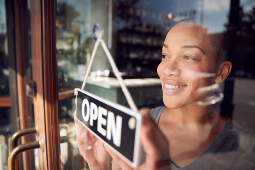 A Black woman turns the open sign on the door of her new business