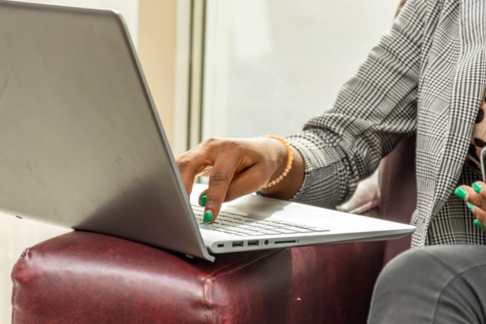A woman uses her laptop while dressed in professional attire and sitting on a sofa