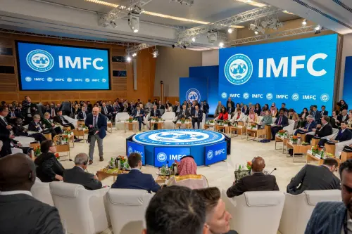 Finance ministers seated in a circle, with screens displaying "IMFC" in the center and behind
