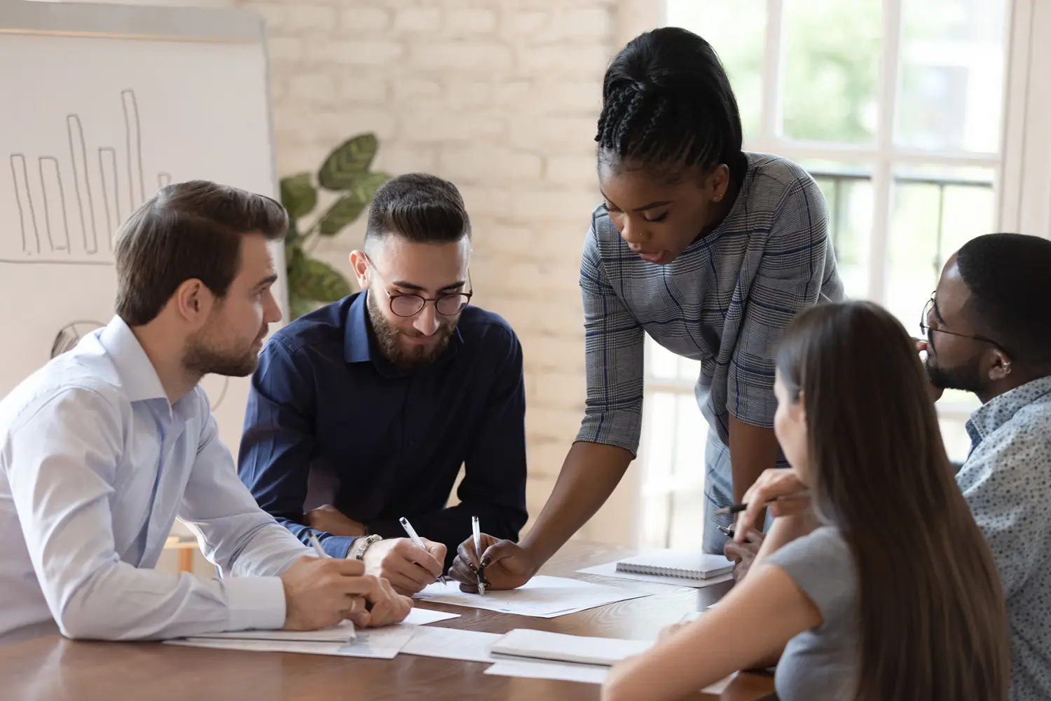 Serious african woman supervisor boss teach diverse staff workers explain project plan paperwork at group meeting, focused black female mentor training business team at corporate office briefing