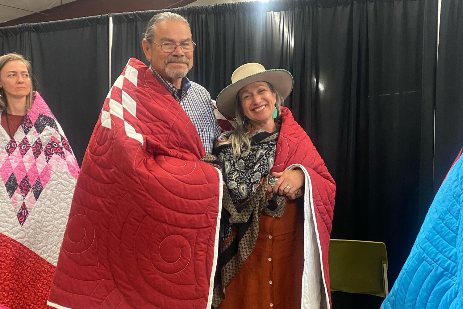 Jael Kampfe, President of Indigenous Impact Co., and Gerald Sherman, Executive Vice President of Indigenous Impact Co., are honored by NACDC for their work with the Coalition by being gifted and wrapped in a star quilt.