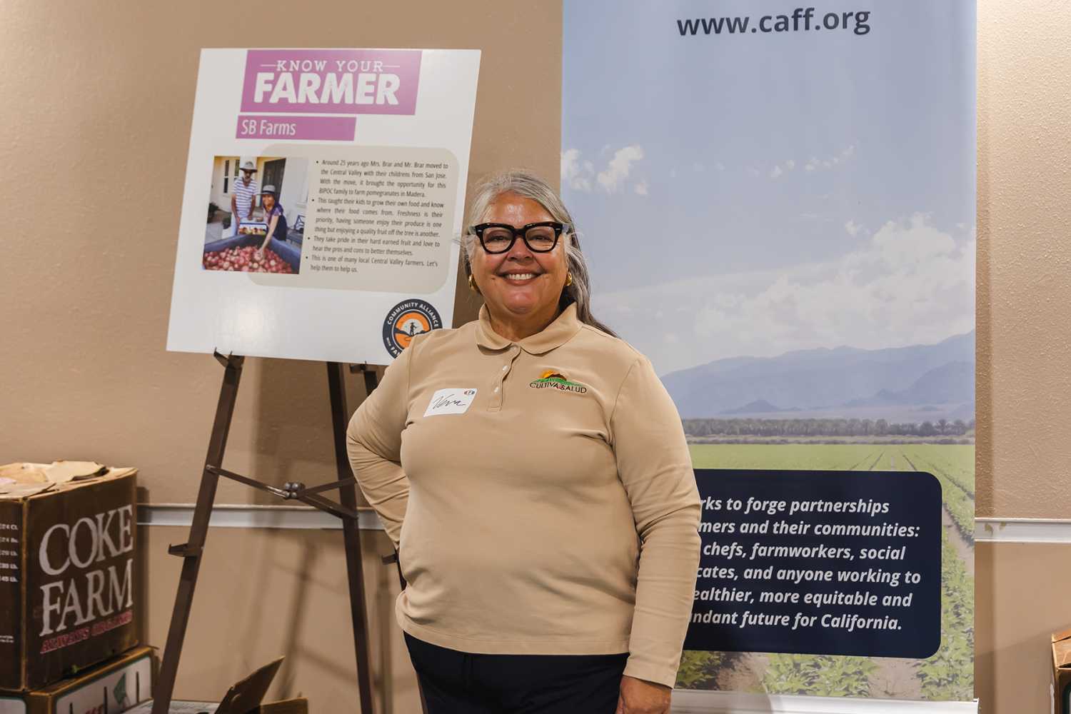 Woman standing behind a table in front of a poster reading "Know your farmer"