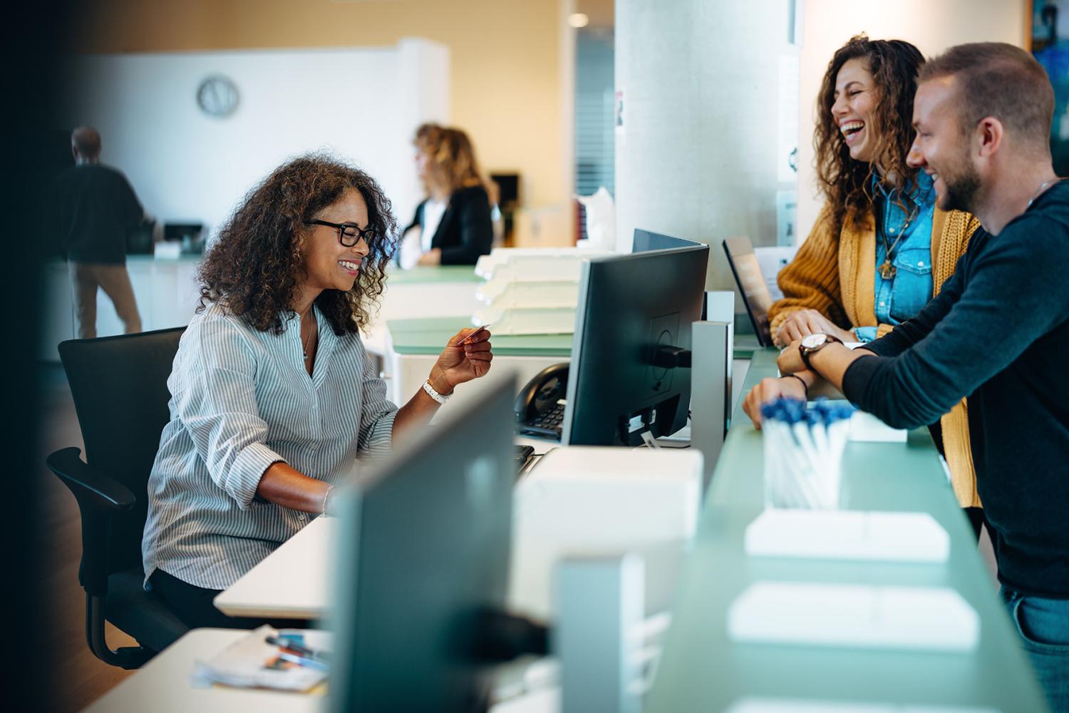 People standing at municipal office reception and talking to a receptionist. Receptionist assisting people standing at front desk.