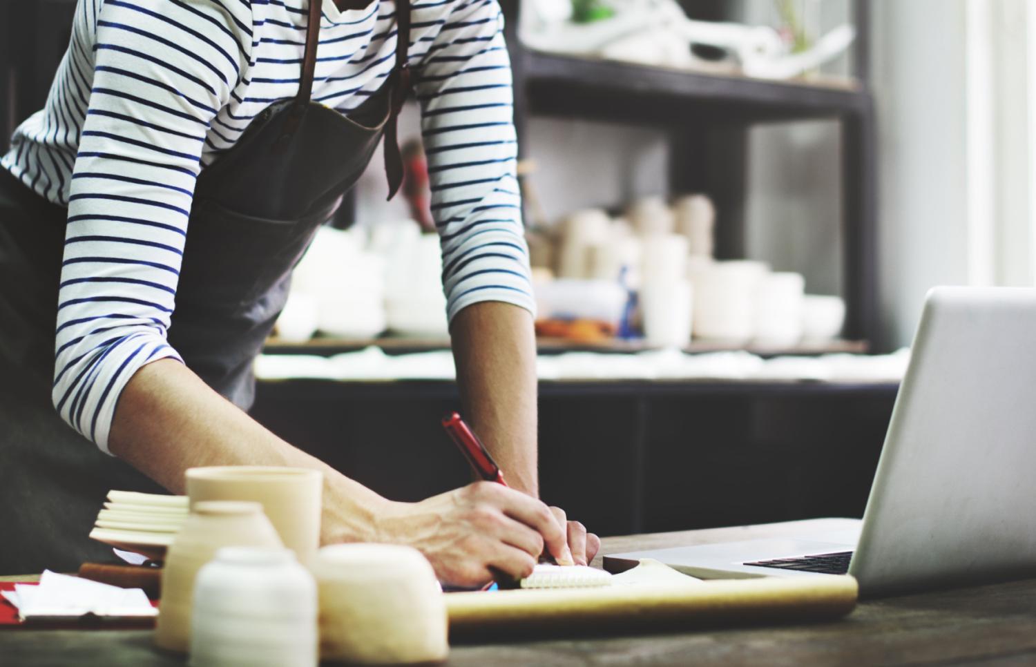 Person in an apron using laptop and making notes.