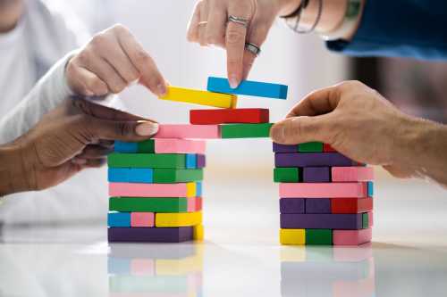 Multiple hands contributing to two columns of building blocks