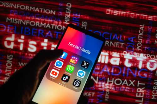 Social media icons logo displayed on a smartphone with disinformation on screen seen in the background, in this photo illustration. On 15 October 2023, in Brussels, Belgium. (Photo illustration by Jonathan Raa/NurPhoto)NO USE FRANCE