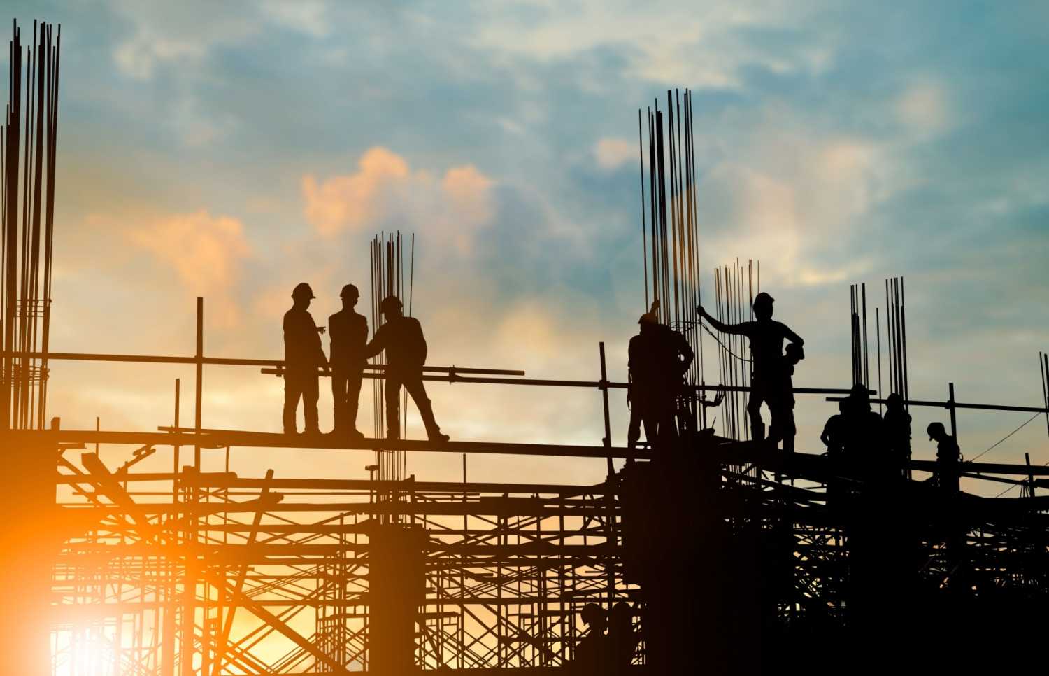 Construction workers on the scaffolding of a partially constructed building, silhouetted against the rising sun