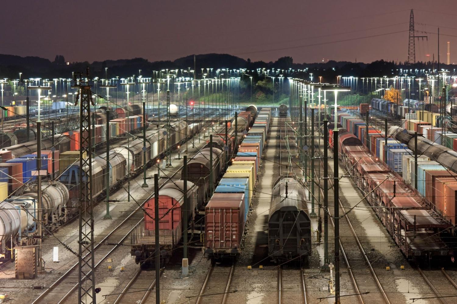 Freight trains sit stationary on tracks in a railyard at night