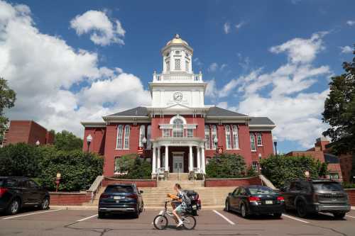 A student carries pizza boxes while riding a bicycle in front of Carver Hall on the Bloomsburg University campus of Commonwealth University of Pennsylvania in Bloomsburg, Pa., on August 13, 2023.