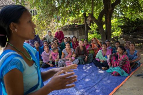 A woman gestures as she speaks to a group of women seated on the ground