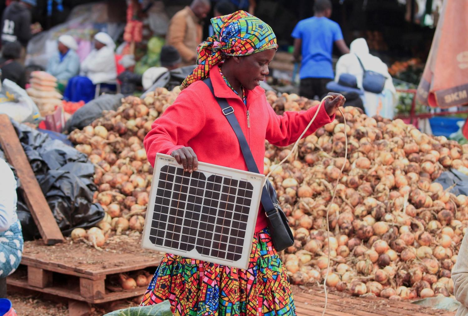 A woman prepares to set up a solar panel to charge her cellphone at a vegetable market in Harare, Zimbabwe, October 2, 2024.