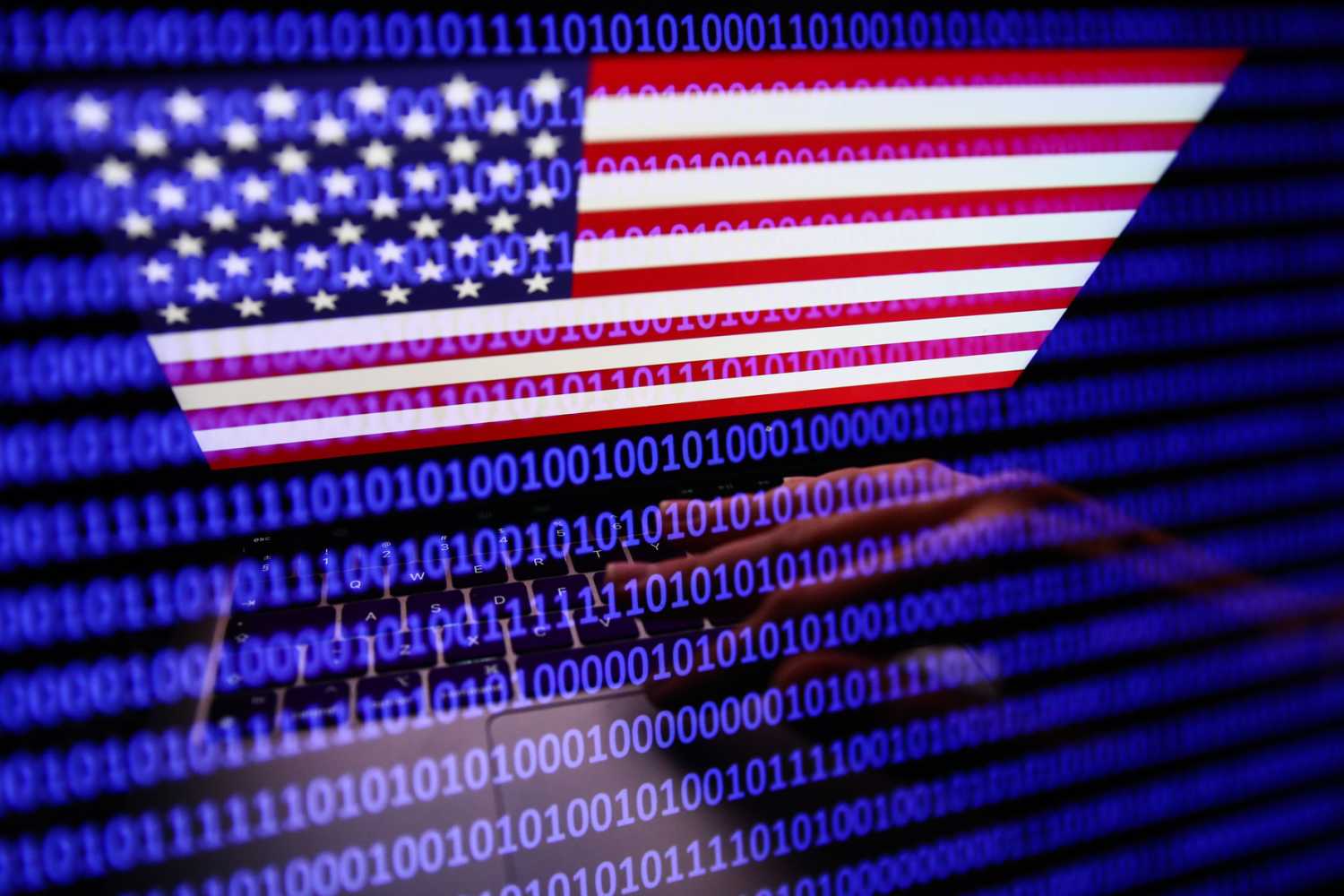 Flag of the United States displayed on a laptop screen and binary code displayed on a screen are seen in this multiple exposure illustration photo taken on September 27, 2022.