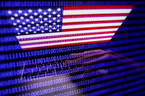 Flag of the United States displayed on a laptop screen and binary code displayed on a screen are seen in this multiple exposure illustration photo taken on September 27, 2022.