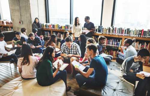 A class of college students in a library, appearing to have broken off into small groups as for a class activity