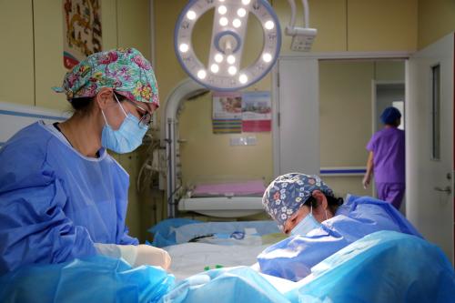 Medical staff wearing masks and gowns assist a woman giving birth in a hospital room