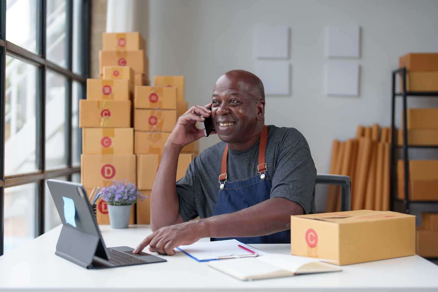 Small Business Startup, SME Owner, American Male Entrepreneur Africans use smartphones and Laptop takes orders and checks online orders to prepare boxes to sell to customers. Online SME business idea