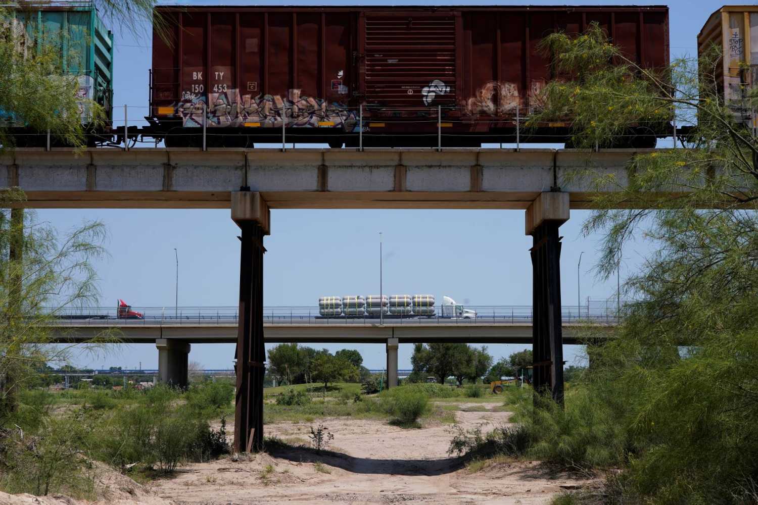 Two bridges over land with a freight train on one and tractor trailers on the other