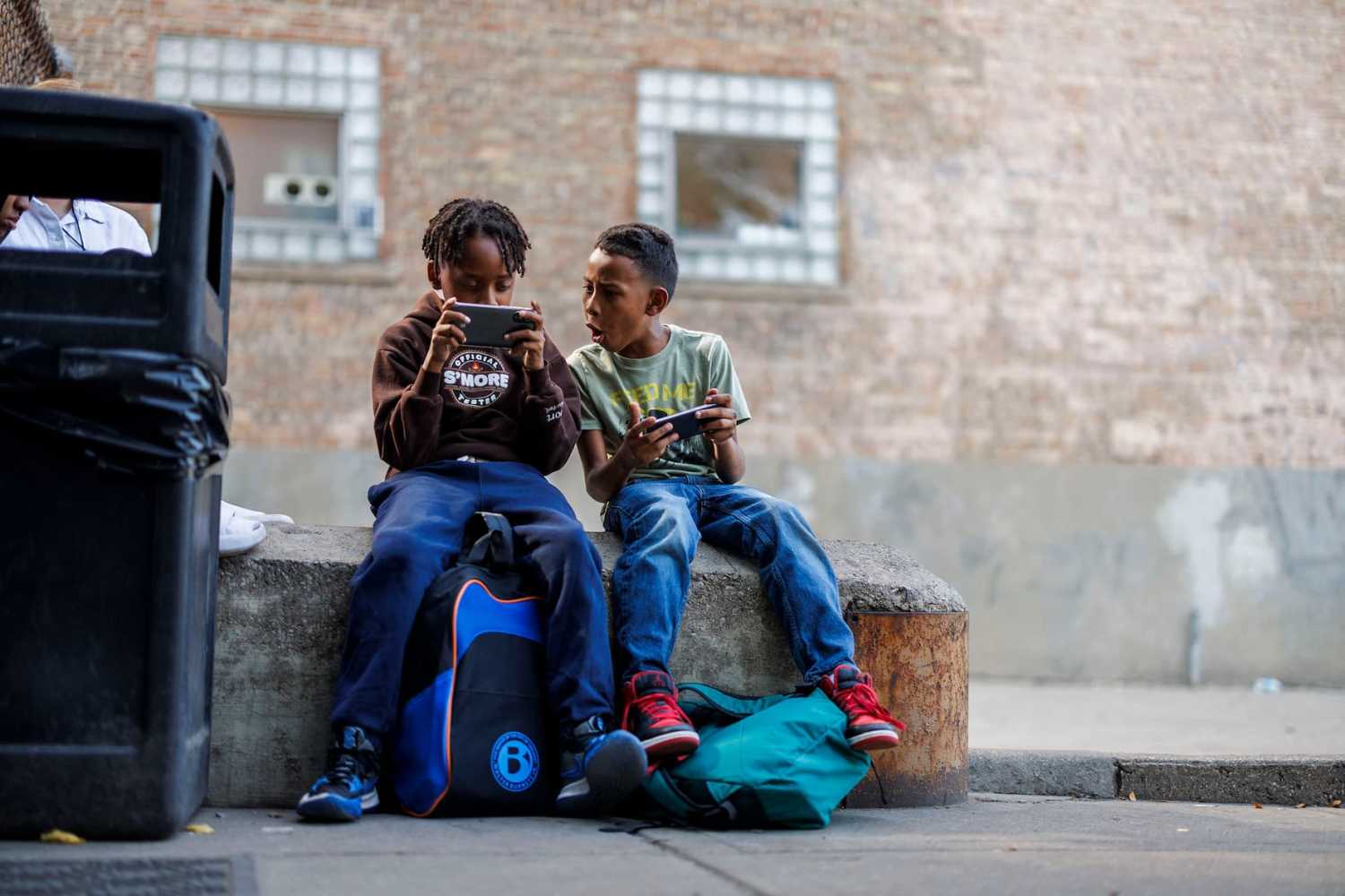 From left, Eduardo Rodriguez, 10, and his brother Andres Gonzalez , 9, both from Venezuela, play with cell phones after coming home from school while sitting outside their shelter on North Ogden Avenue Monday Sept. 9, 2024, in Chicago. Recently the city announced it would close the migrant shelter on North Ogden Avenue.