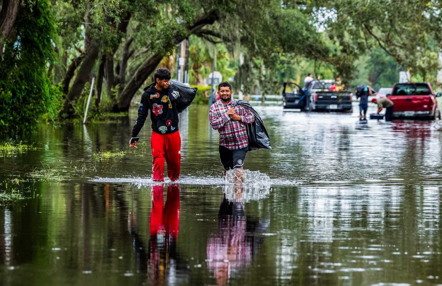 Juan Jose Muñoz, left, and Elvin Antonio Urbina walk with their belongings through a flooded street in North Tampa, Florida, on Thursday, Oct. 10, 2024, a day after Hurricane Milton crossed Florida’s Gulf Coast.