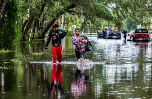 Juan Jose Muñoz, left, and Elvin Antonio Urbina walk with their belongings through a flooded street in North Tampa, Florida, on Thursday, Oct. 10, 2024, a day after Hurricane Milton crossed Florida’s Gulf Coast.