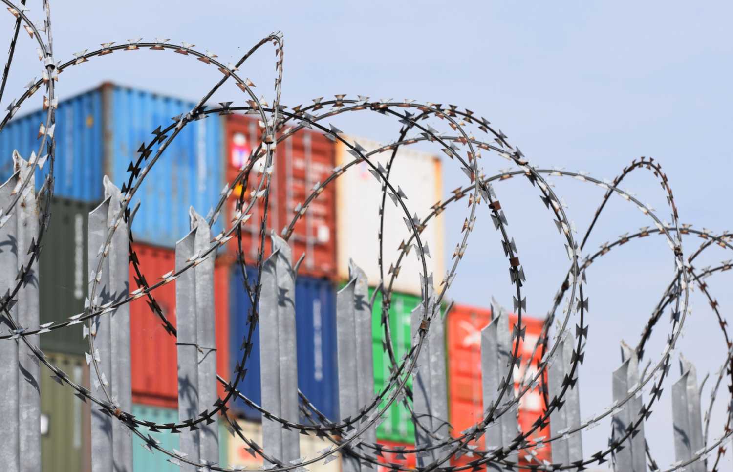 Shipping containers behind a barbed wire fence.