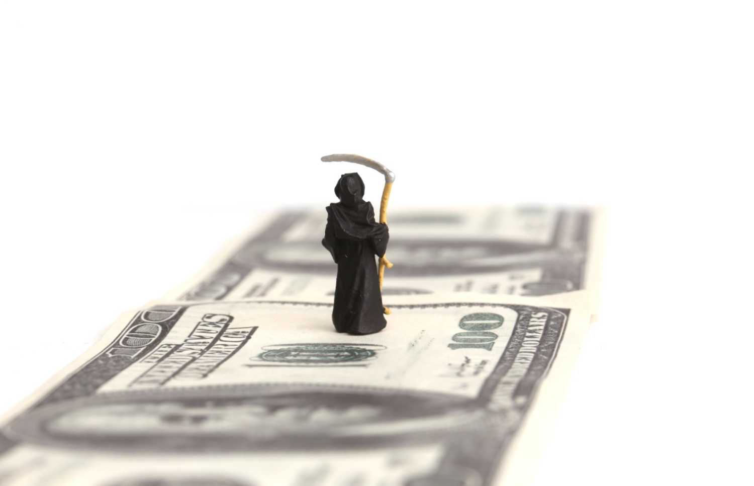 Grim reaper figurine standing on a $100 bill