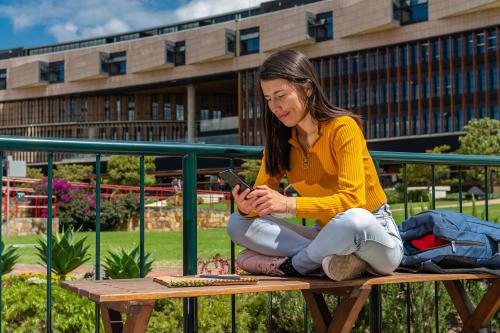 Native American woman, student, sitting on a college campus bench while checking her mobile phone