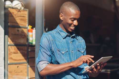 A man uses a tablet while standing in front of a shelf full of boxes